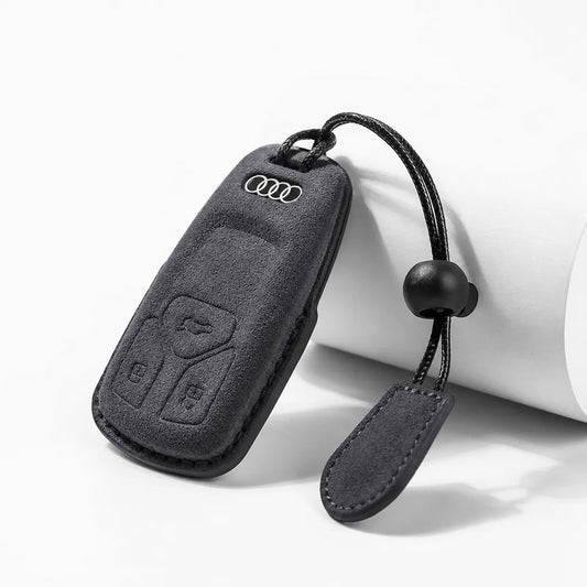 Dark Charcoal suede car key fob cover with an embossed Audi logo and button cutouts, shown on a white background with a cylindrical prop.