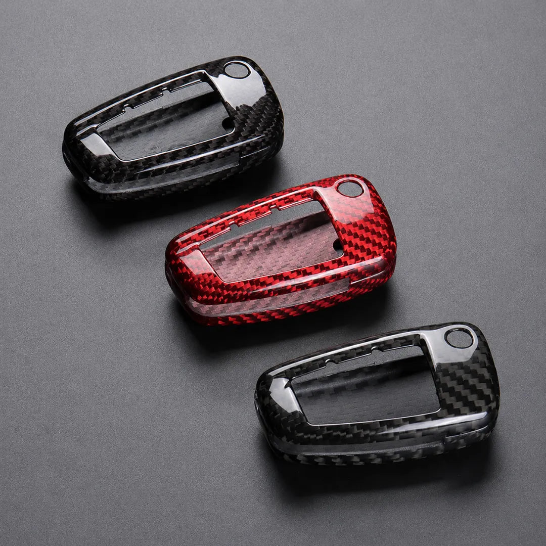 Three glossy carbon fiber key fob covers in black and red, arranged diagonally on a dark gray background.