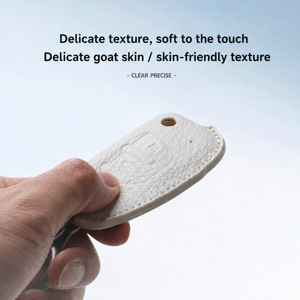 A hand holding a small white leather key fob cover with a key partially inserted, against a light blue gradient background with text describing the delicate goat skin texture.