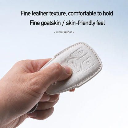 A hand holding a white leather car key fob cover with button engravings, set against a light blue gradient background with promotional text about fine leather texture and goatskin feel.