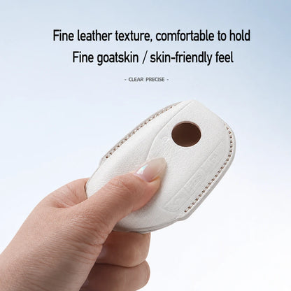 A hand holding a white leather car key fob cover with a circular cutout, against a light blue gradient background with promotional text about fine leather texture and goatskin feel.