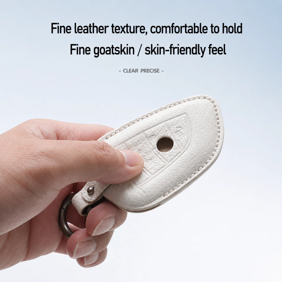 A hand holding a cream-colored leather key fob cover with a metal key ring, set against a light blue gradient background with descriptive text at the top.