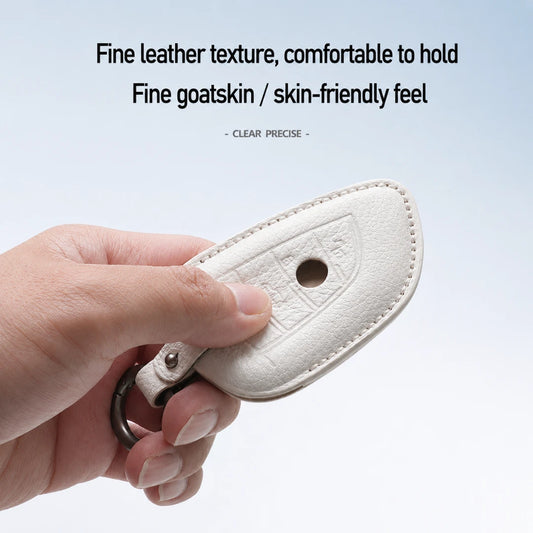 A hand holding a cream-colored leather key fob cover with a metal key ring, set against a light blue gradient background with descriptive text at the top.