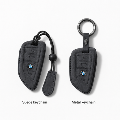 Two BMW keychain covers shown side by side on a light gray background: a suede keychain on the left with a black cord and bead, and a metal keychain on the right with a round key ring. Text below labels them 'Suede keychain' and 'Metal keychain'.