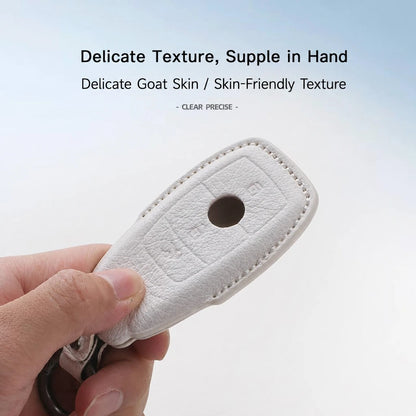 A hand holding a white textured key fob cover made of goat skin or a similar material, with text above describing its delicate texture and skin-friendly quality.