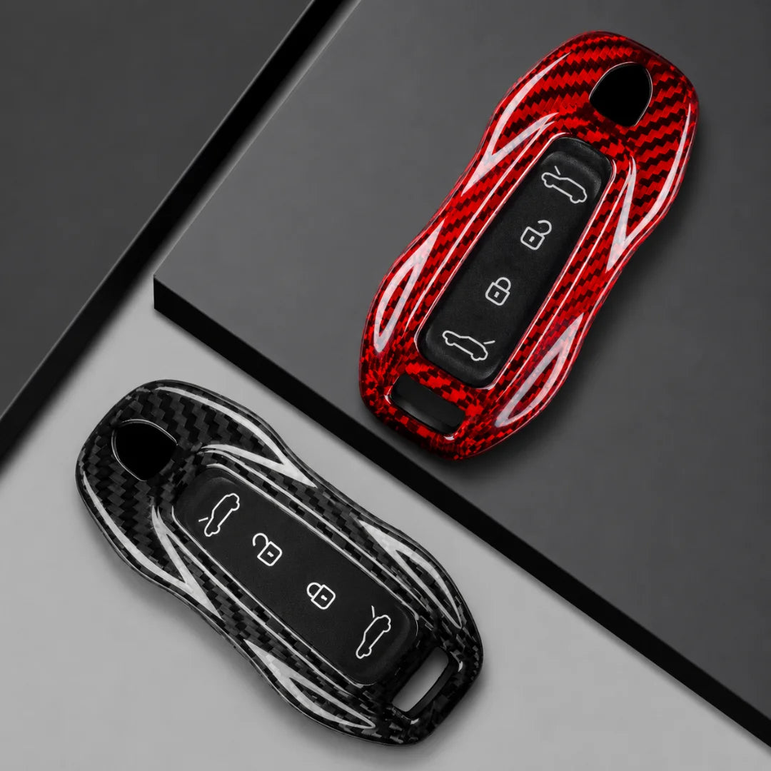 Two glossy key fob covers displayed on a dark gray geometric background. One cover is red with a carbon-fiber-style pattern and white curved accents, and the other is black with a carbon-fiber-style pattern and white curved accents.