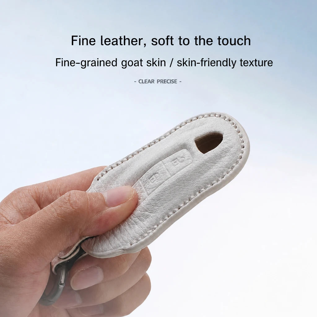 A hand holding a light beige leather key fob cover or keychain case, with text above describing the fine leather and soft goat skin texture.