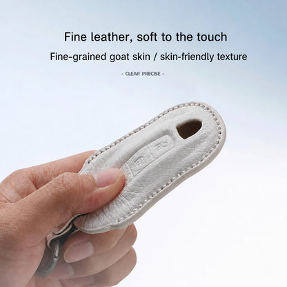 A hand holding a light beige leather key fob cover or keychain case, with text above describing the fine leather and soft goat skin texture.