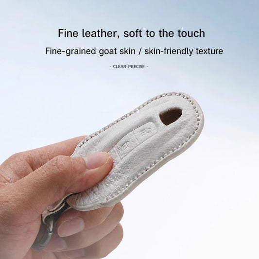 A hand holding a light beige leather key fob cover or keychain case, with text above describing the fine leather and soft goat skin texture.