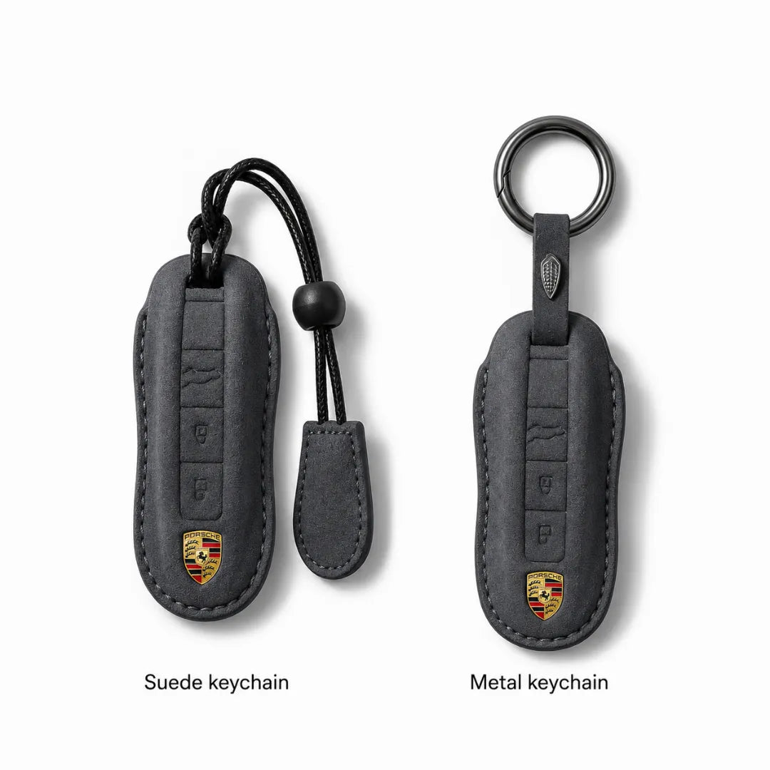 Two Porsche keychain covers shown on a light gray background, labeled 'Suede keychain' and 'Metal keychain.' The left version is suede-like dark gray with a black strap and a small Porsche crest near the bottom.