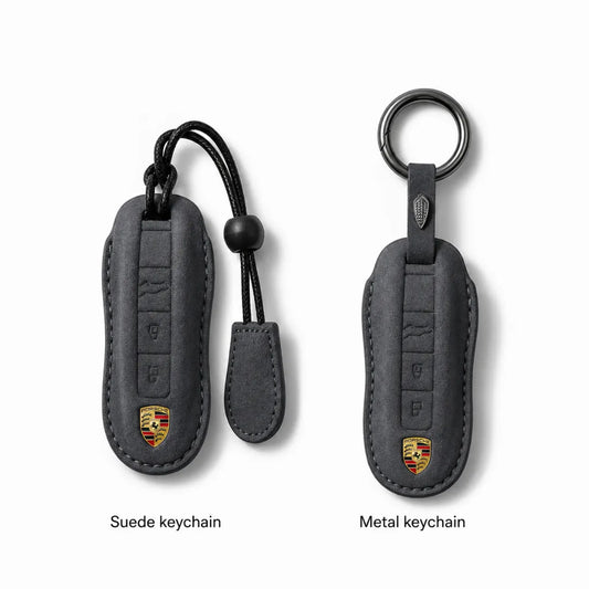 Two Porsche keychain covers shown on a light gray background, labeled 'Suede keychain' and 'Metal keychain.' The left version is suede-like dark gray with a black strap and a small Porsche crest near the bottom.