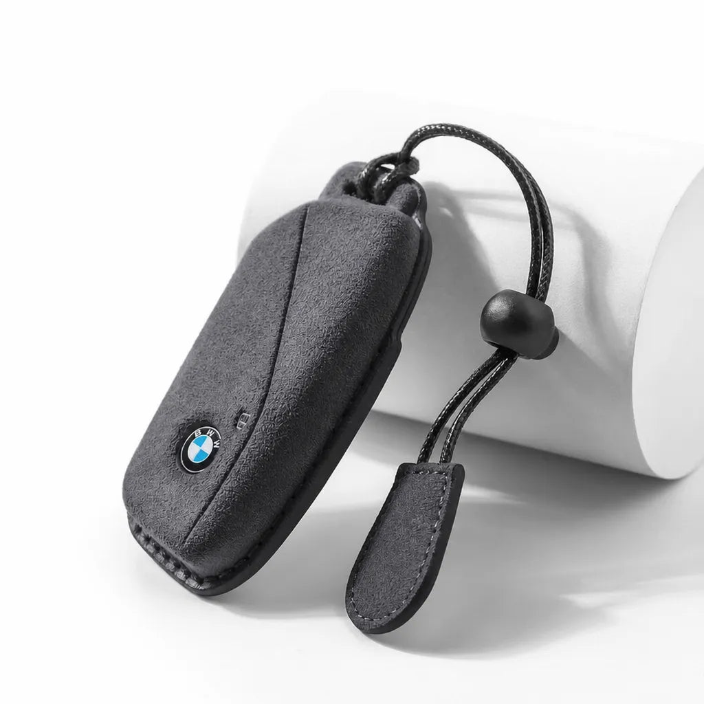 A black textured car key fob cover with a small BMW logo, shown on a white cylindrical prop against a white background.