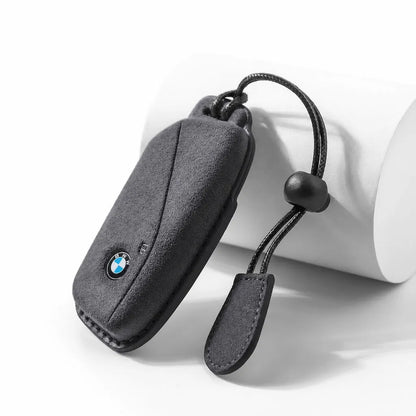 A black textured car key fob cover with a small BMW logo, shown on a white cylindrical prop against a white background.