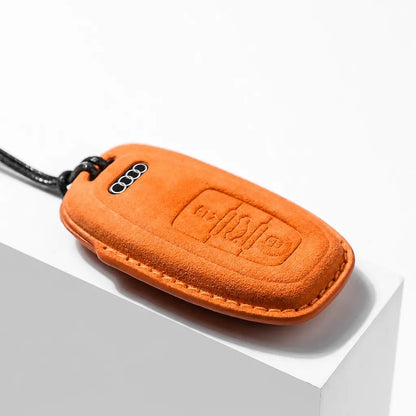 An orange suede car key fob cover with a black lanyard, shown resting on a white geometric display block.