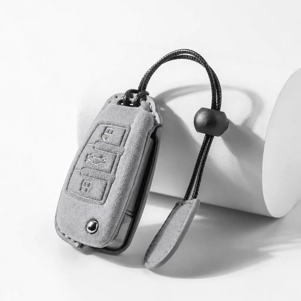 A light gray suede car key fob cover with a black braided strap and black rubber bead, shown on a clean white studio background.