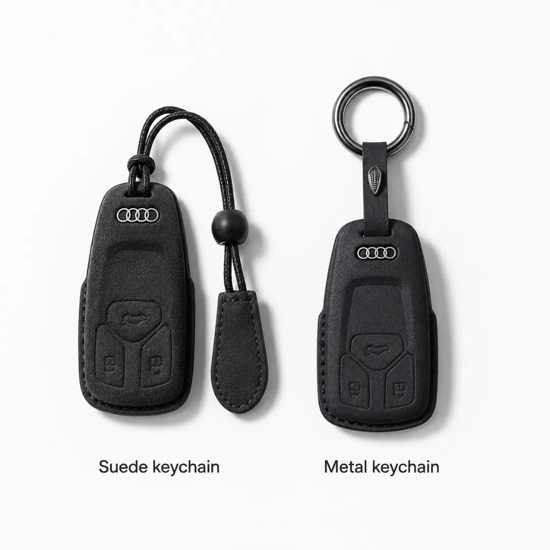 Two Audi keychain covers shown side by side on a light gray background: a suede keychain on the left with a black cord and tab, and a metal keychain on the right with a ring. Text below reads 'Suede keychain' and 'Metal keychain'.