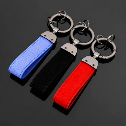 Three fabric keychains in blue, black, and red, each with a silver metal key ring and clip, arranged diagonally on a dark reflective surface.