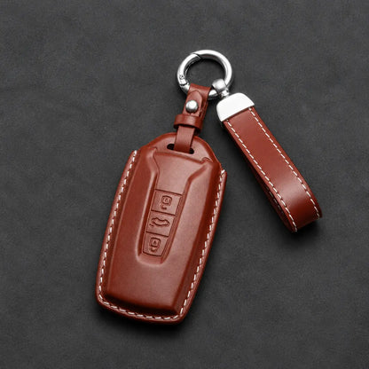 A brown leather car key fob cover with white contrast stitching, a silver metal key ring, and a matching leather keychain strap, displayed on a dark textured background.