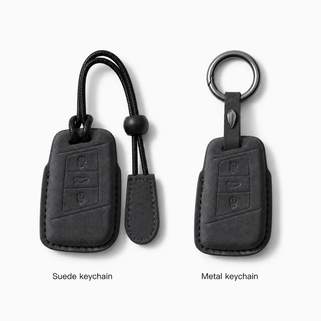 Two black car keychain covers shown side by side on a light gray background, labeled 'Suede keychain' and 'Metal keychain.' The left version has a black cord and toggle, and the right version has a metal ring and black strap.