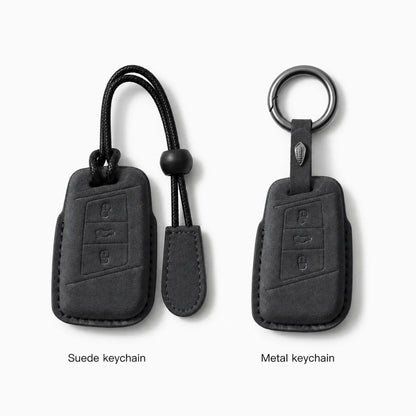 Two black car keychain covers shown side by side on a light gray background, labeled 'Suede keychain' and 'Metal keychain.' The left version has a black cord and toggle, and the right version has a metal ring and black strap.