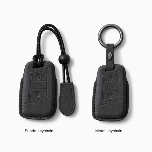 Two black car keychain covers shown side by side on a light gray background, labeled 'Suede keychain' and 'Metal keychain.' The left version has a black cord and toggle, and the right version has a metal ring and black strap.