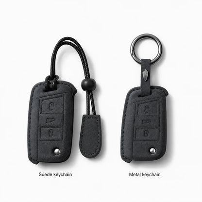 Two car keychain covers shown on a light gray background: a suede black keychain on the left with a black cord and bead, and a metal keychain on the right with a silver ring and tab. Text below reads 'Suede keychain' and 'Metal keychain'.